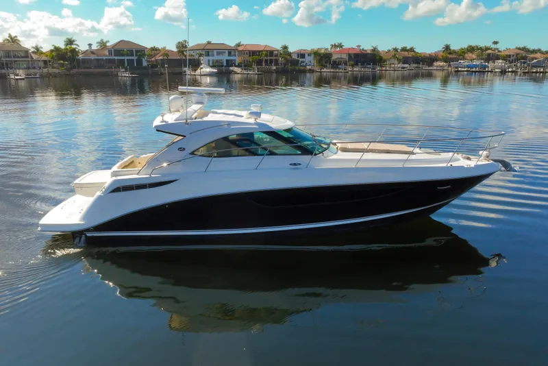 Slide: The Image of 2015 Sea Ray 410 Sundancer yacht on calm water, with scenic waterfront homes. - 6