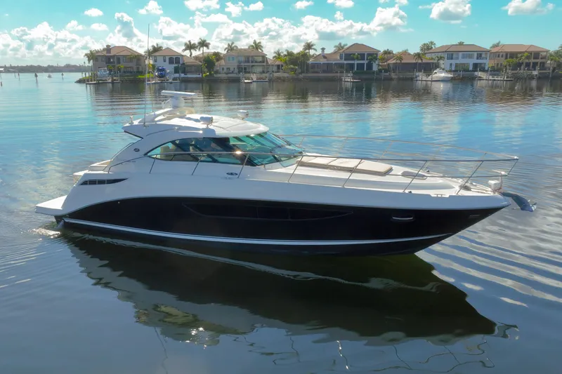 Slide: The Image of 2015 Sea Ray 410 Sundancer yacht on calm water with waterfront homes in background. - 7