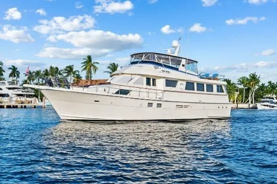 Slide: The Image of 1989 Hatteras 70 Motor Yacht on calm water under a blue sky with palm trees. - 2