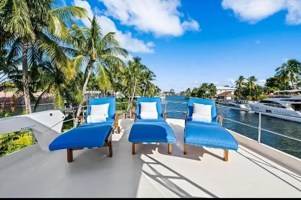 Slide: The Image of 1989 Hatteras 70 Motor Yacht deck with blue loungers, palm trees, and waterfront view. - 32