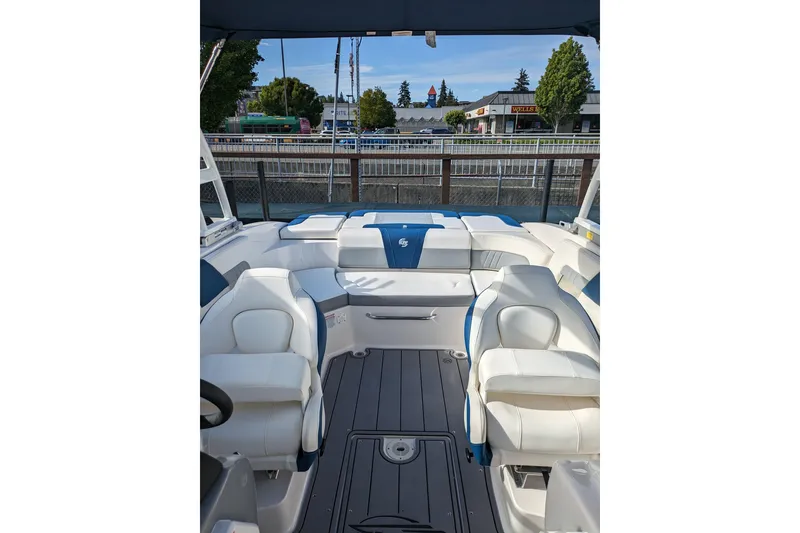 Slide: The Image of 2023 Chaparral 23 Surf boat interior with white and blue seating, docked near a cityscape. - 6