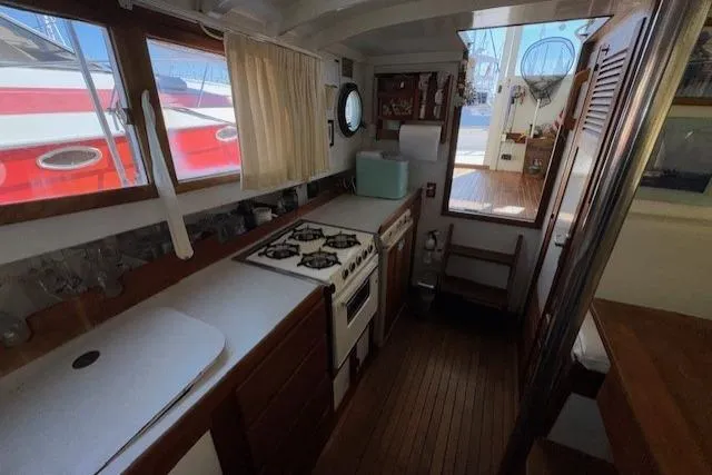 Slide: The Image of Interior of 1980 Roughwater MOTOR SAILER, featuring a compact kitchen with stove and wooden cabinetry. - 10