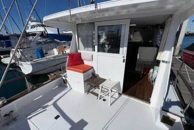Slide: The Image of 1980 Roughwater MOTOR SAILER deck with seating, docked at marina under clear blue sky. - 14