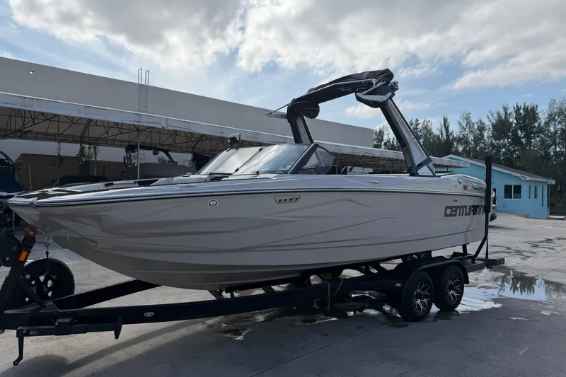 Slide: The Image of 2026 Centurion Nv233 boat on trailer, parked outdoors under cloudy sky. - 2