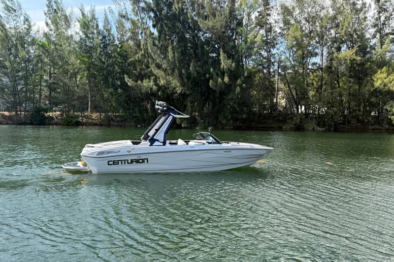 Slide: The Image of 2026 Centurion Nv233 boat cruising on a serene lake with lush trees in the background. - 23