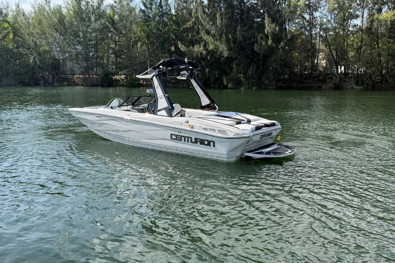 Slide: The Image of 2026 Centurion Nv233 boat on a serene lake with lush trees in the background. - 26