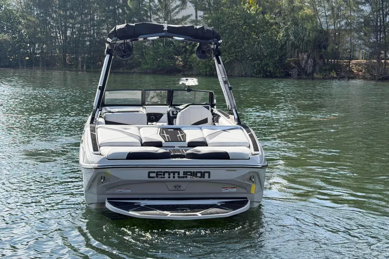 Slide: The Image of 2026 Centurion Nv233 boat on calm water, rear view with lush greenery background. - 27