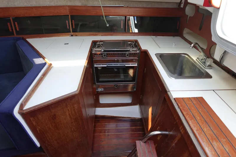 Slide: The Image of 1987 Hunter 310 yacht kitchen with stove, sink, and wooden cabinetry. - 25