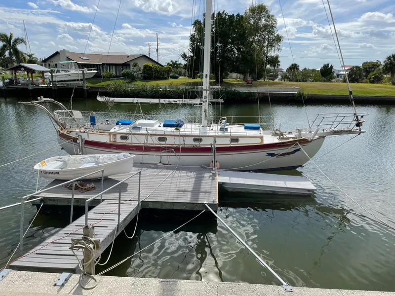 The Image of 1985 Tayana 37 Cutter sailboat docked on a calm canal under a partly cloudy sky. - 0