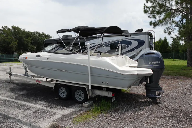 The Image of 2022 Stingray 231 DC boat on trailer with Yamaha outboard motor, parked outdoors. - 0