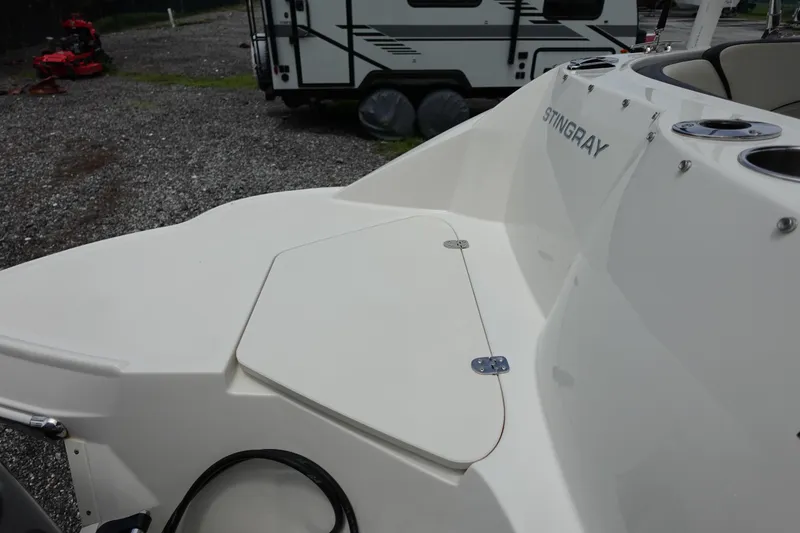 Slide: The Image of 2022 Stingray 231 DC boat deck with storage compartment, parked near a trailer. - 16