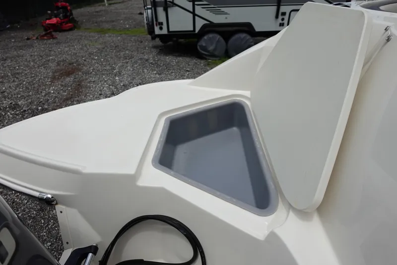 Slide: The Image of 2022 Stingray 231 DC boat storage compartment with open lid, gravel background. - 17