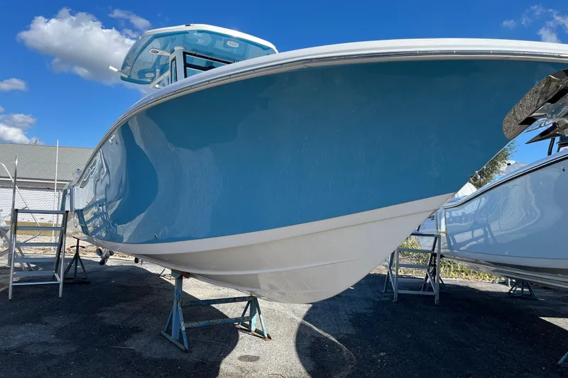 Slide: The Image of 2026 Tidewater 272 CC Adventure boat with blue hull on stands, under clear sky. - 2