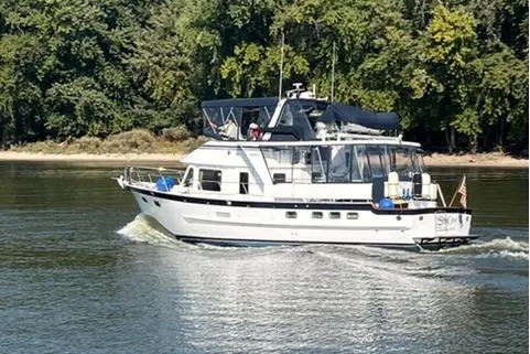 Slide: The Image of 2005 DeFever 49 Cockpit Motor Yacht cruising on a calm river with lush green trees. - 3