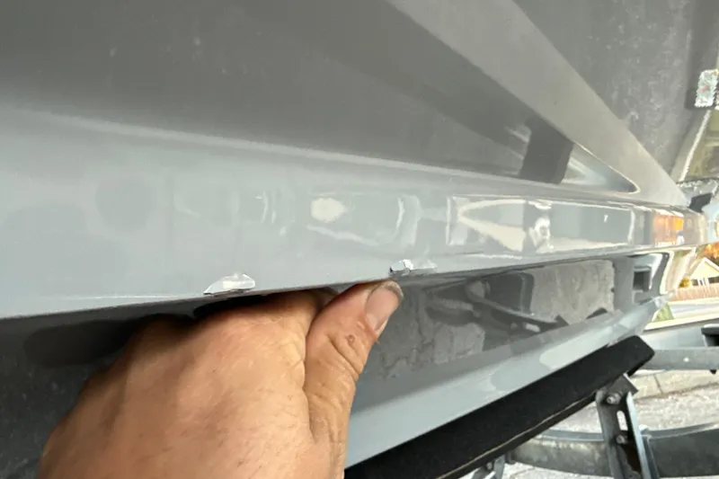 Slide: The Image of Close-up of 2023 NauticStar 2602 Legacy boat hull with visible chips and hand inspecting. - 60