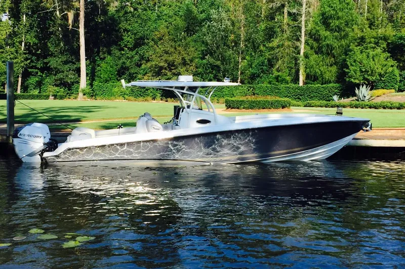 The Image of 2014 Nor-Tech 340 Sport Center Console boat docked by lush greenery. - 0