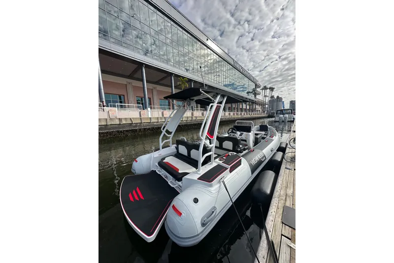 Slide: The Image of 2026 Highfield 660 Velox boat docked by a modern building under a cloudy sky. - 2