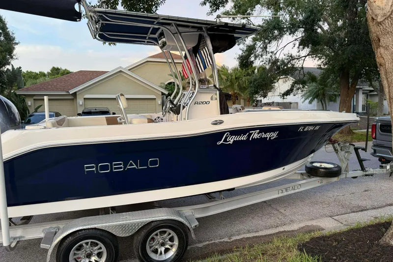 Slide: The Image of 2017 Robalo R200ES boat on trailer, named "Liquid Therapy," parked in residential area. - 2