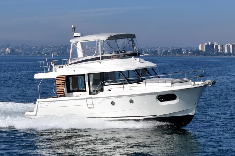 Slide: The Image of 2025 Beneteau Swift Trawler 41 cruising on open water, cityscape in background. - 56