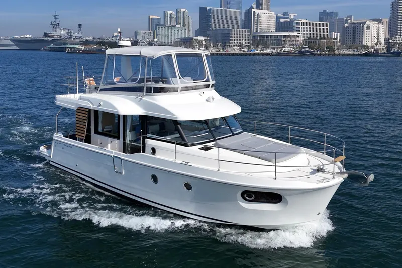 Slide: The Image of 2025 Beneteau Swift Trawler 41 cruising in urban harbor with city skyline backdrop. - 58