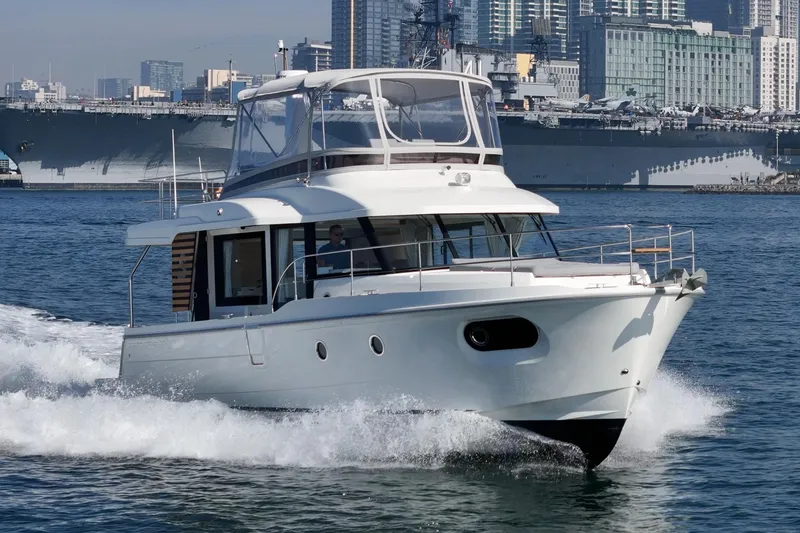 Slide: The Image of 2025 Beneteau Swift Trawler 41 cruising in urban harbor with city skyline backdrop. - 76