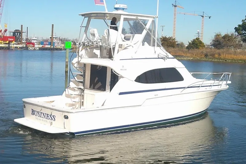 Slide: The Image of 2005 Bertram 390 Convertible yacht cruising on a calm river with industrial backdrop. - 3