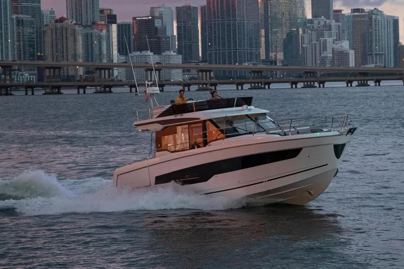 Slide: The Image of 2024 Jeanneau NC 1295 Fly yacht deck with seating and table, docked by waterfront homes. - 12