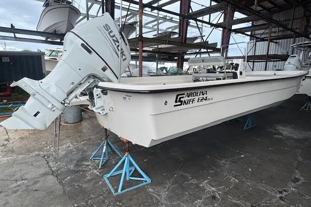The Image of 2026 Carolina Skiff E24 DLX CC boat with Suzuki outboard motor in storage. - 1