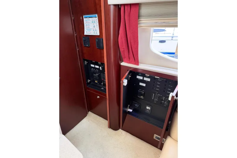 Slide: The Image of Electrical panel inside 2004 Sea Ray 480 Sedan Bridge yacht, featuring wood cabinetry and red curtains. - 40