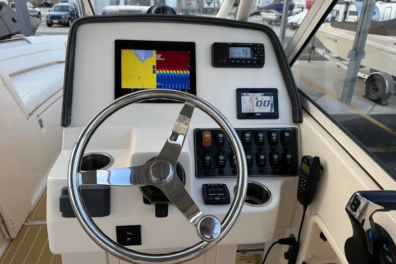 Slide: The Image of 2022 Grady-White Freedom 235 boat dashboard with steering wheel and navigation controls. - 22