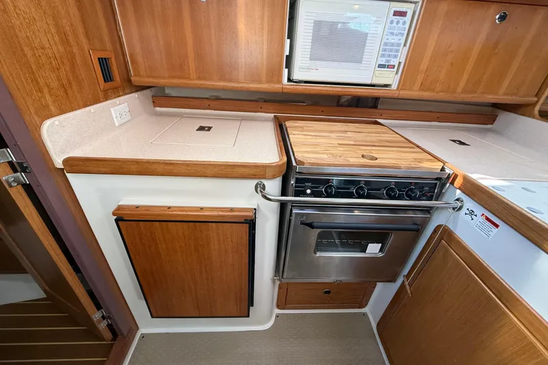 Slide: The Image of 1999 Catalina 380 yacht kitchen with stove, microwave, and wooden cabinetry. - 49