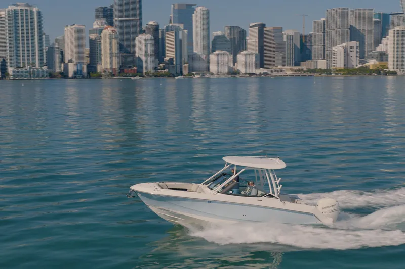 The Image of 2022 Boston Whaler 240 Vantage cruising on water with city skyline backdrop. - 0