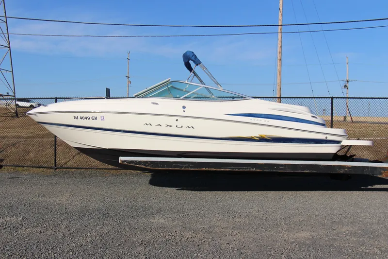 The Image of 2004 Maxum 2400 SR boat on trailer, parked near a chain-link fence. - 0