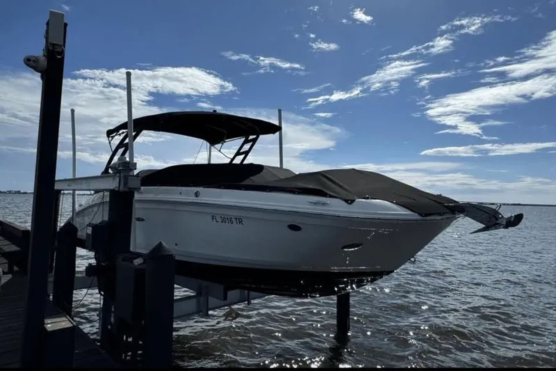 The Image of 2024 Sea Ray SDX 270 boat with black cover on a lift by the water. - 0