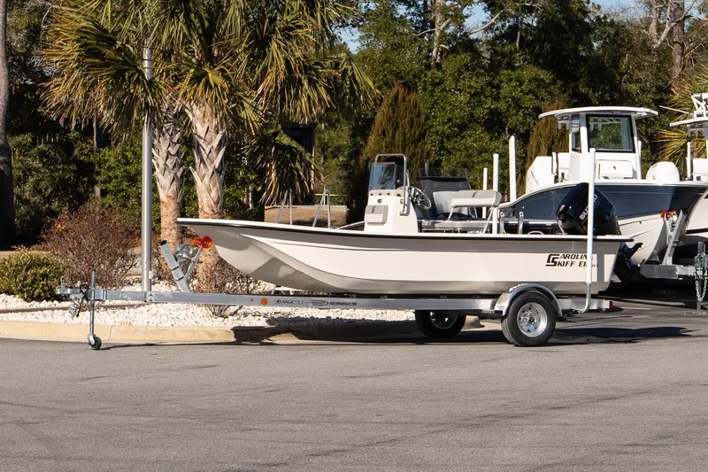 The Image of 2026 Carolina Skiff E18 JVX CC boat on trailer, parked outdoors near palm trees. - 1