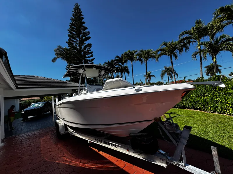 Slide: The Image of 2004 Robalo R 260 boat on trailer in driveway, surrounded by palm trees. - 1