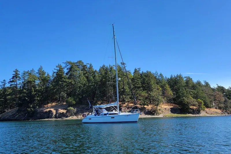Slide: The Image of Sailboat Hunter 336 (1995) on calm water near a forested shoreline under clear blue sky. - 3