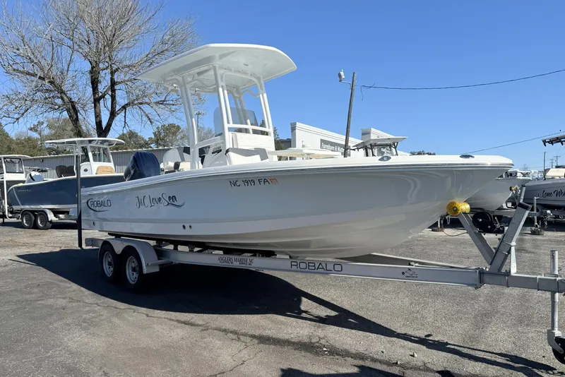 The Image of 2023 Robalo 226 Cayman boat on trailer, parked outdoors under clear blue sky. - 0