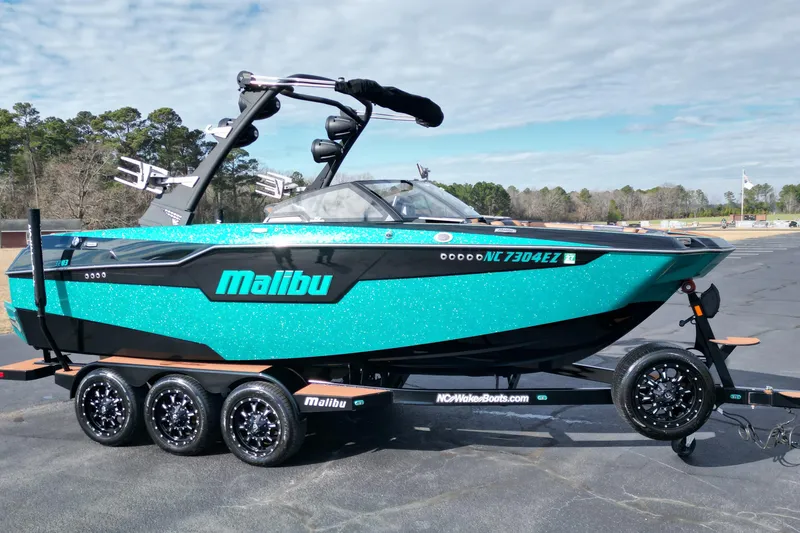 The Image of 2023 Malibu M220 boat on trailer, vibrant turquoise color, parked outdoors. - 1