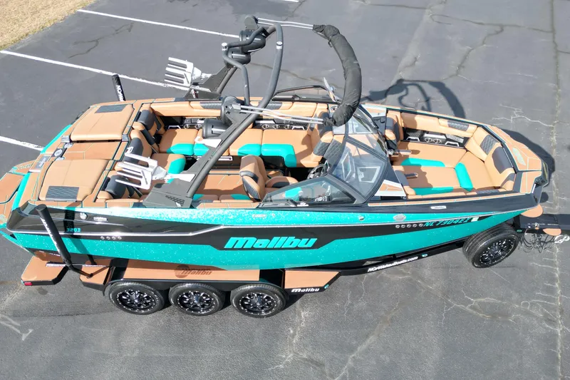 Slide: The Image of 2023 Malibu M220 boat with teal and tan interior, parked on pavement. - 17