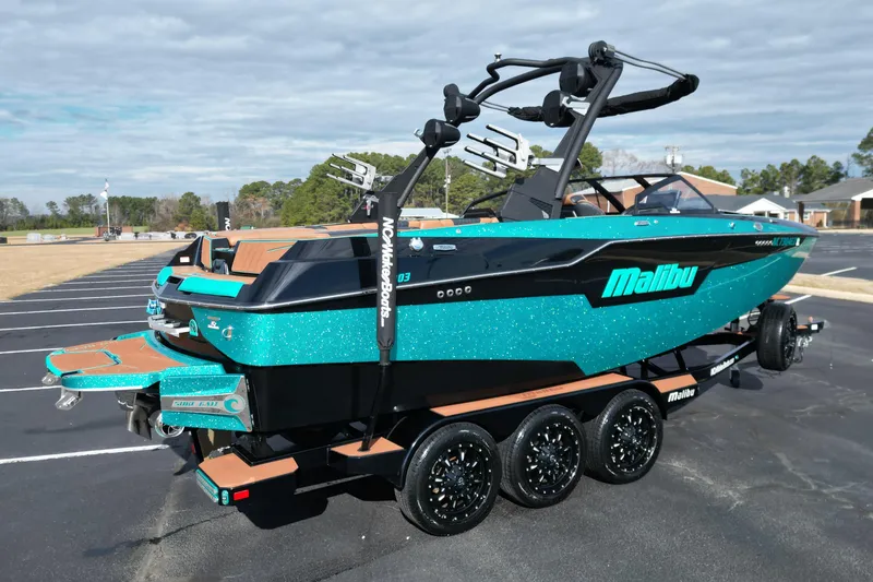 Slide: The Image of 2023 Malibu M220 boat with vibrant teal finish on a trailer in a parking lot. - 3