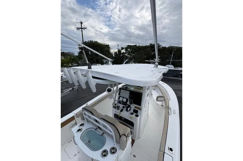 Slide: The Image of 2023 Sea Pro 259 DLX boat cockpit with helm, rod holders, and seating under cloudy sky. - 6