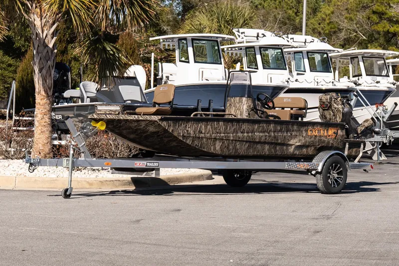Slide: The Image of 2026 Excel 1860 Shallow Water F4 CC boat on trailer, parked outdoors. - 2