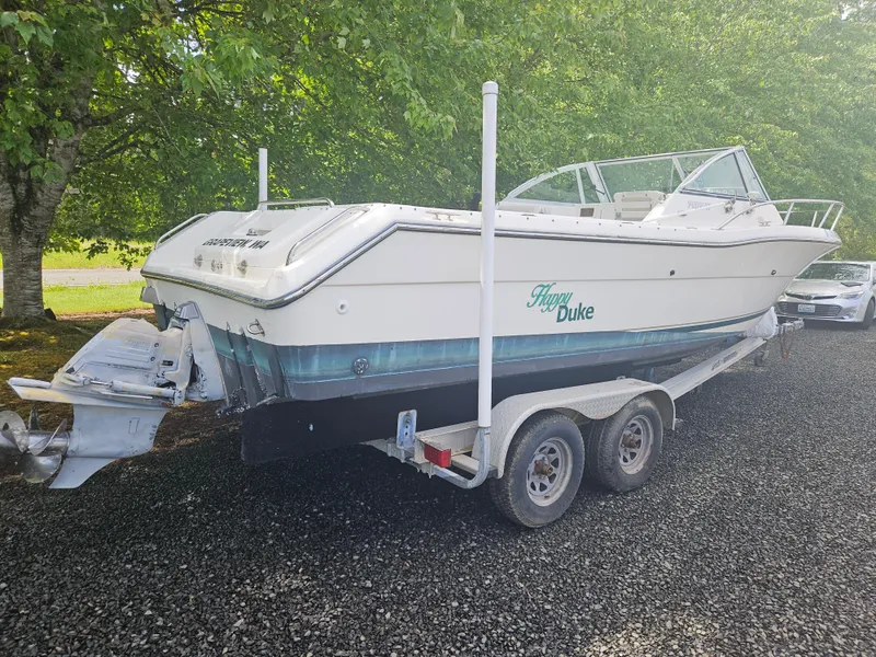 Slide: The Image of 1999 Pursuit 2460 Denali boat on trailer, parked on gravel, surrounded by trees. - 3