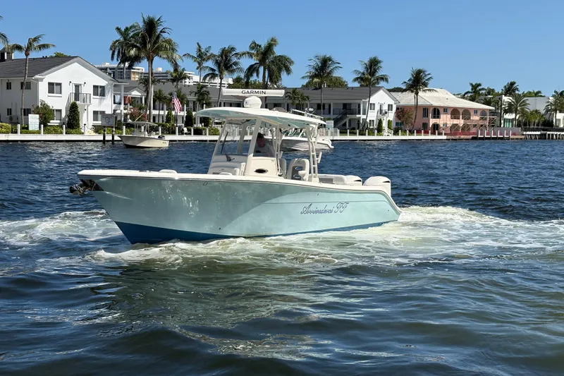 Slide: The Image of 2018 Cobia 301 Center Console boat cruising on a sunny waterfront with palm trees. - 1