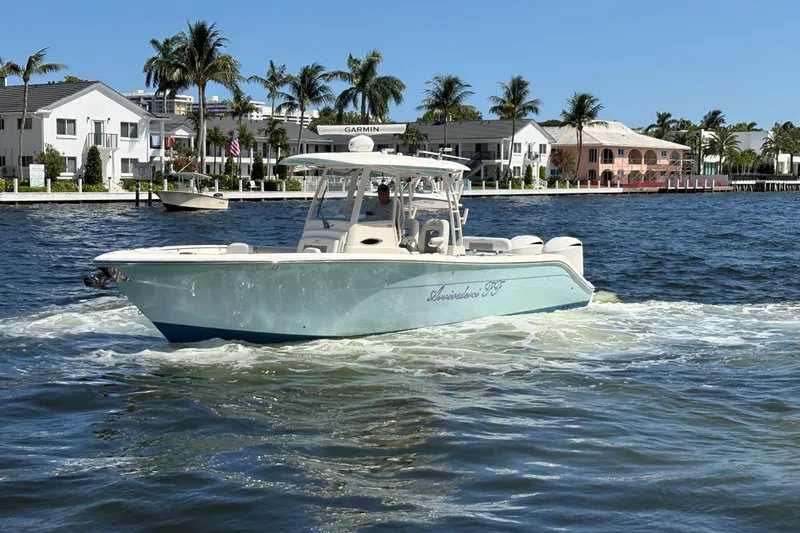 Slide: The Image of 2018 Cobia 301 Center Console boat cruising on a sunny waterfront with palm trees. - 2