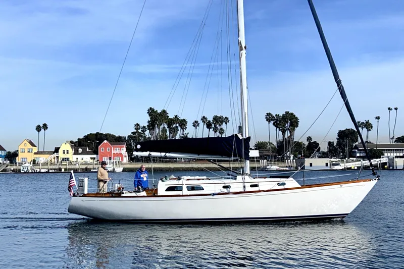 The Image of 1969 Hinckley 38 sailboat on calm water with colorful houses and palm trees in the background. - 0