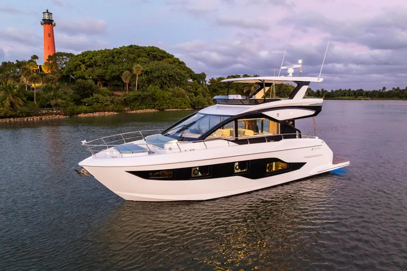 Slide: The Image of 2026 Cruisers 50 Fly yacht on serene water near a lighthouse at sunset. - 7