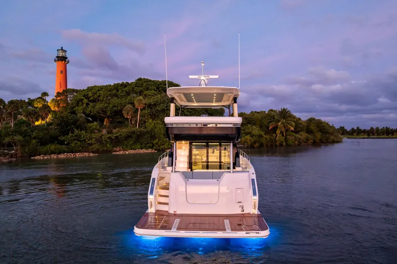 Slide: The Image of 2026 Cruisers 50 Fly yacht illuminated at dusk near a lighthouse and lush greenery. - 47