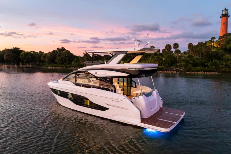 Slide: The Image of 2026 Cruisers 50 Fly yacht at sunset near a lighthouse, serene water setting. - 8